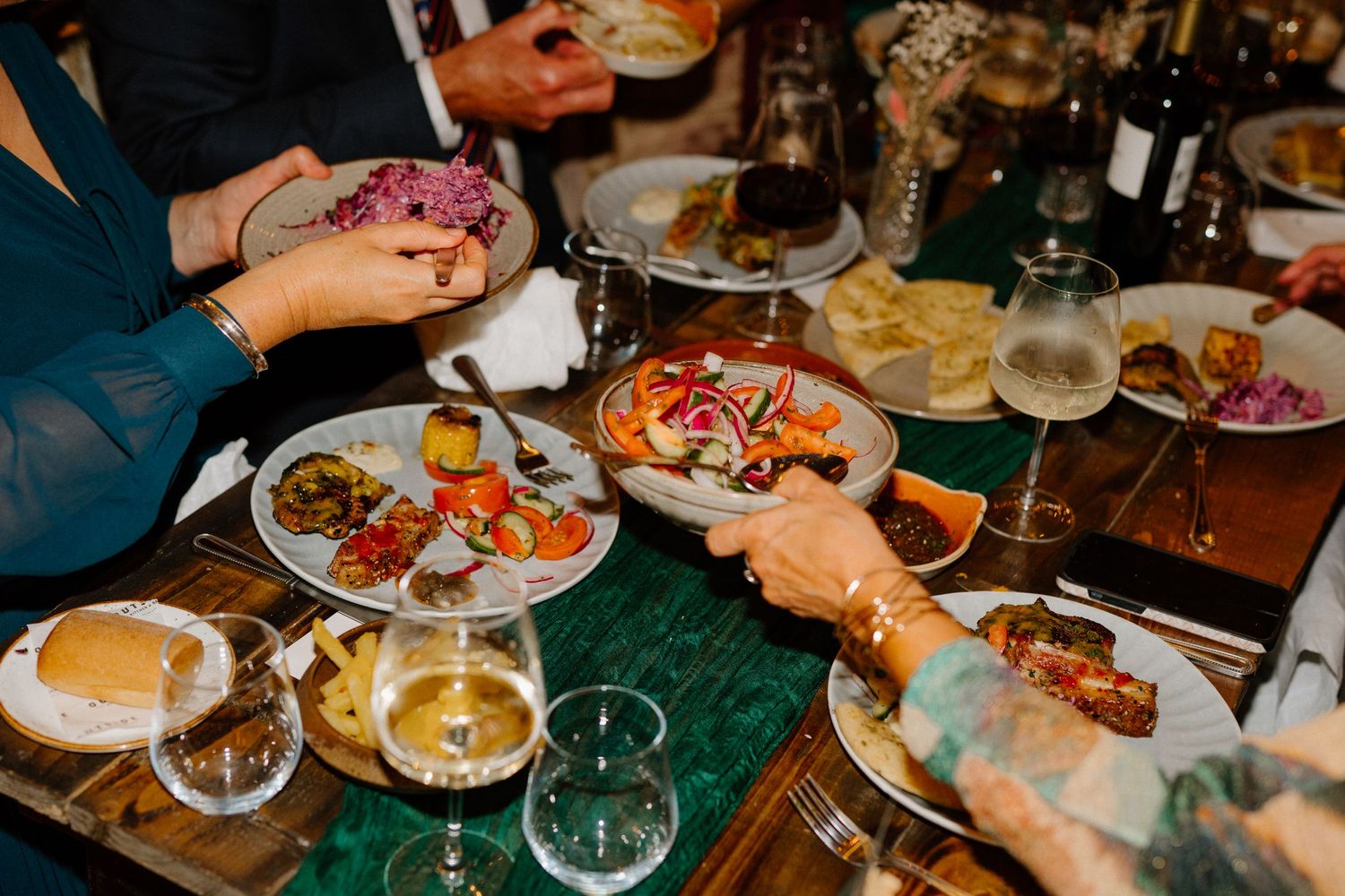 A dining table with shared plates of food and beverages showing hands reaching for various dishes at a restaurant.