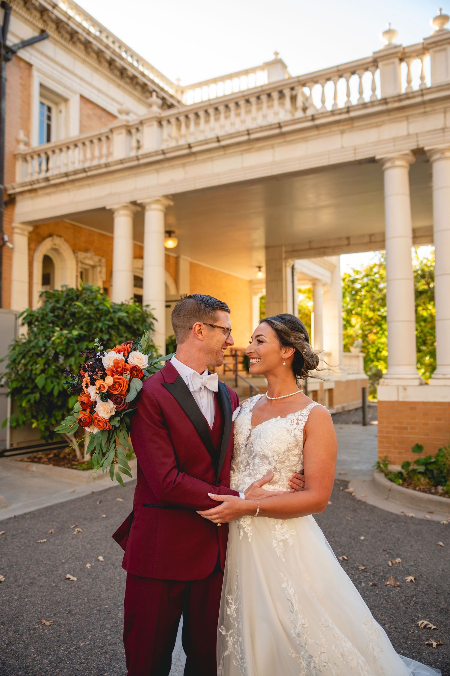 Elegant wedding portrait outside a grand colonial style building with white columns at golden hour.
