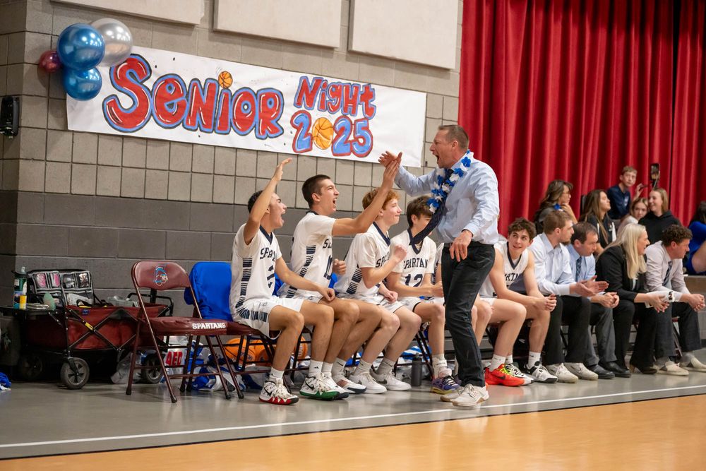 Coach Brent Hanson celebrates with NPA basketball players sit on the sidelines during a game at the Senior Night event.