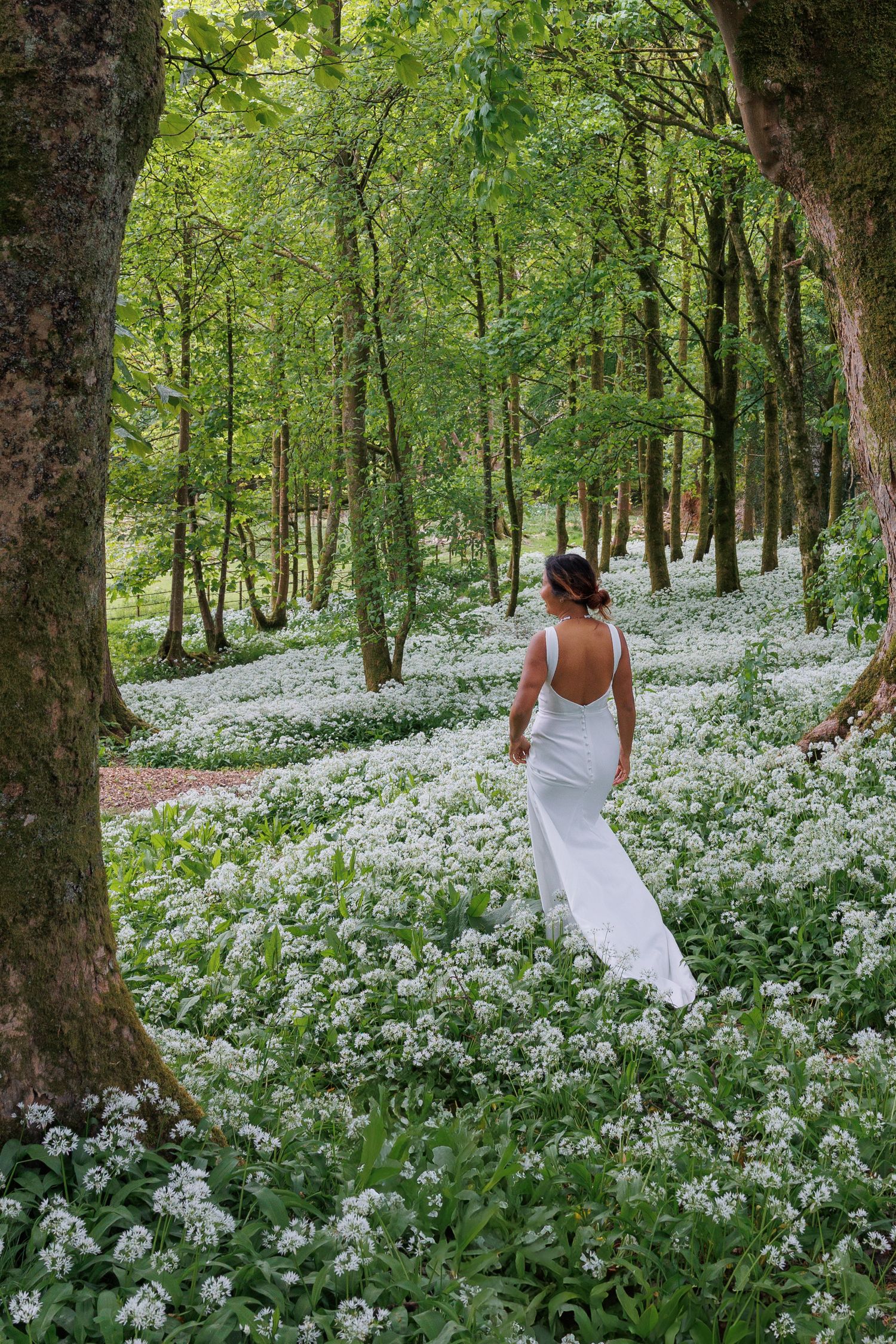 White-gowned figure walks through forest floor covered in blooming wild garlic flowers.