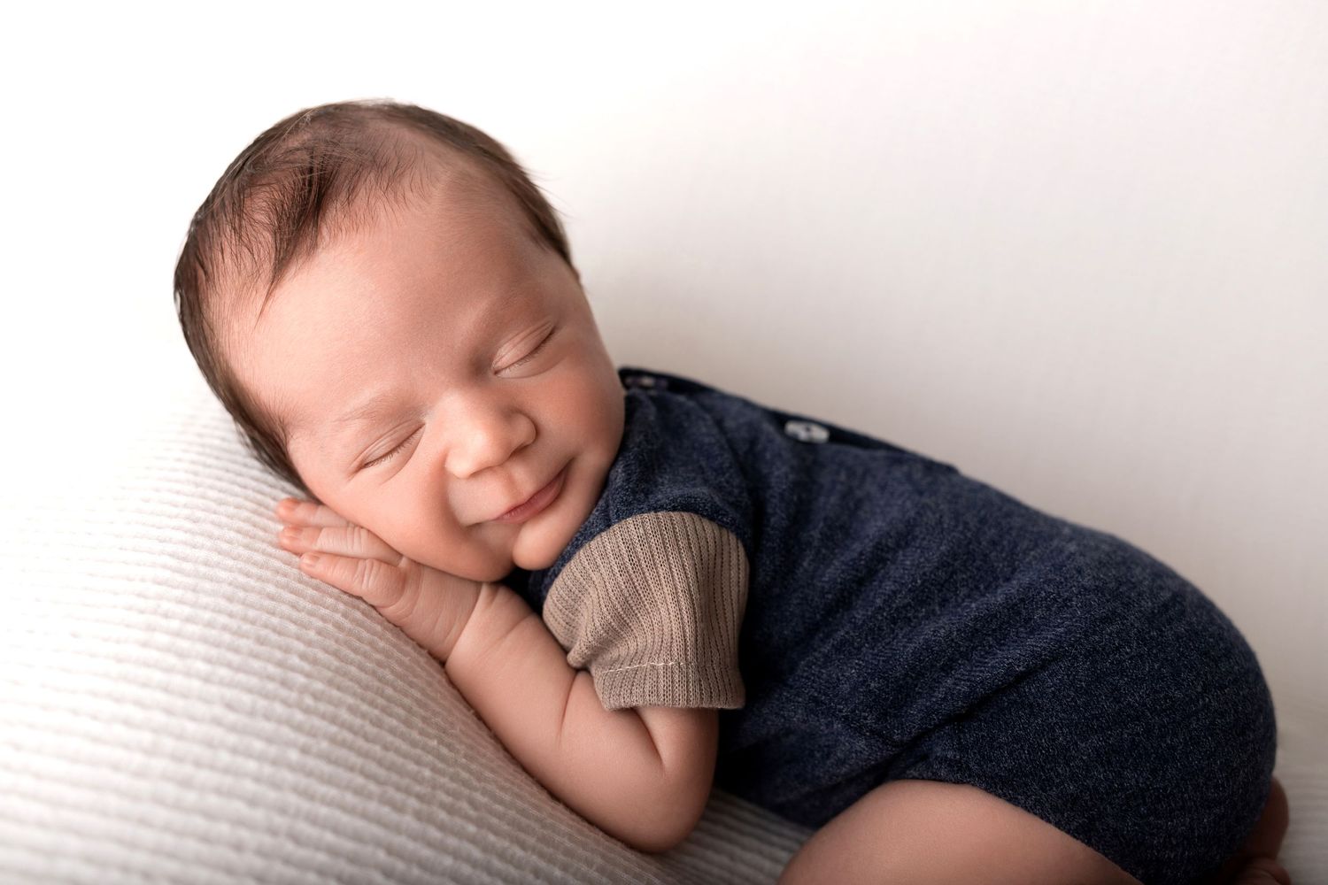 Sleeping baby in navy outfit resting on white pillow with peaceful expression.