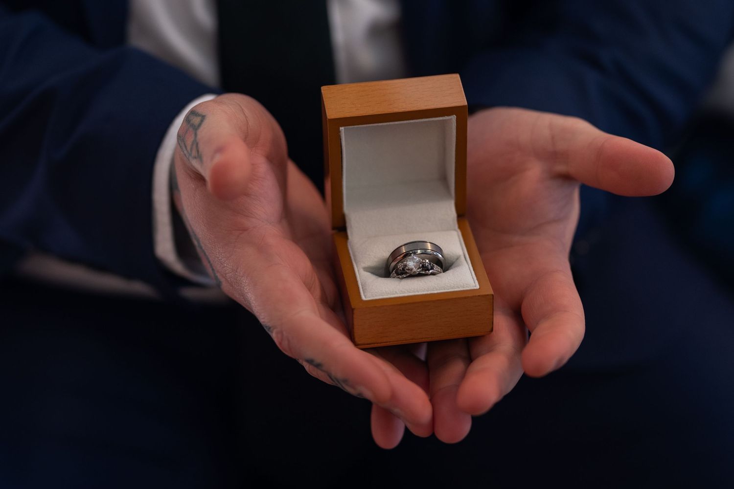Hands holding small wooden jewelry box against navy blue background.