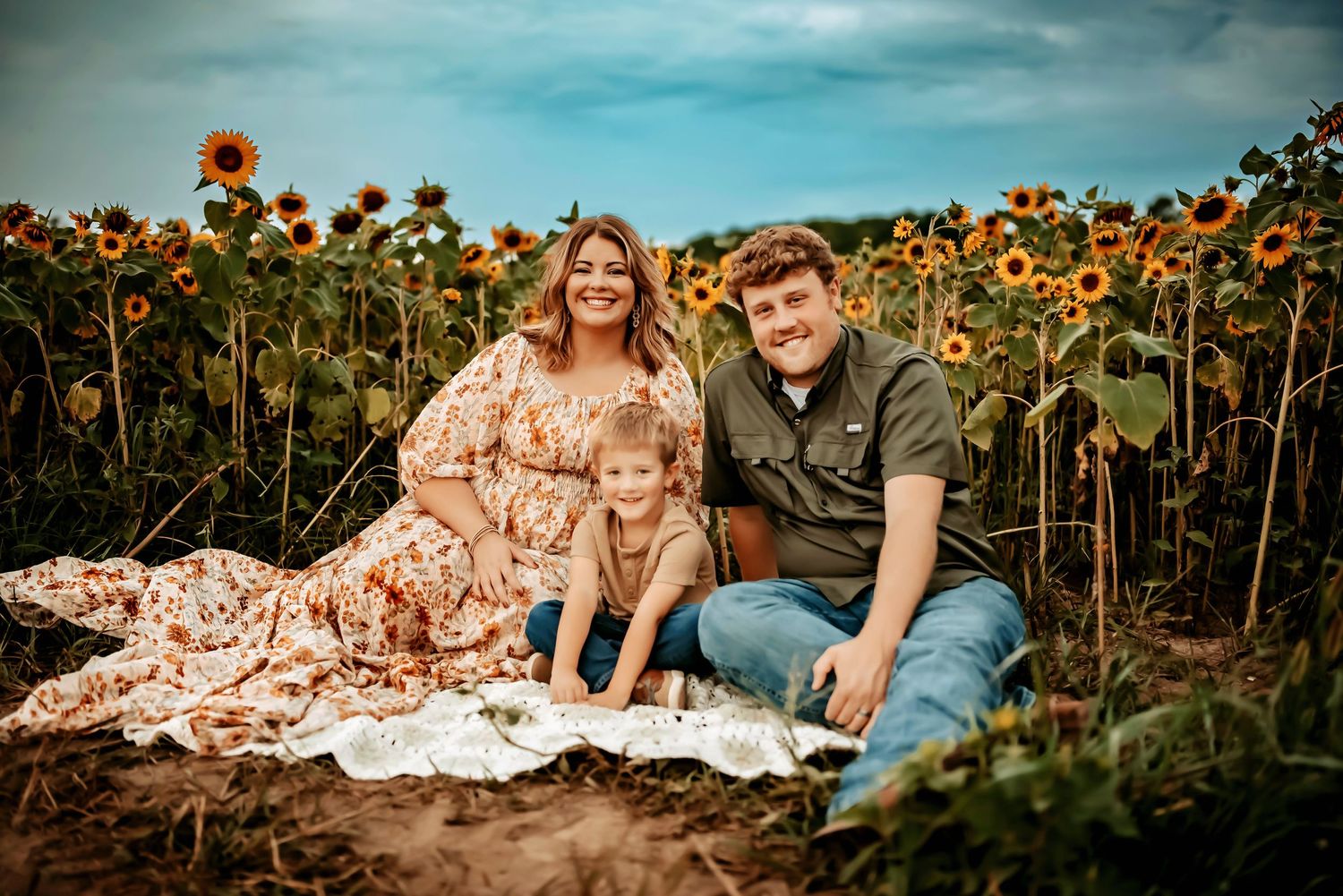 A couple sits together on a blanket in a vibrant sunflower field during a golden hour photoshoot.