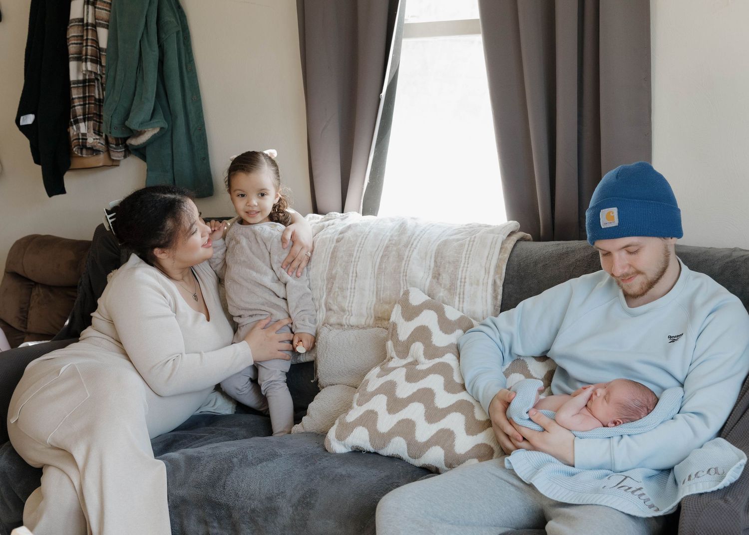 Family relaxing together in living room on grey couch with decorative chevron pillow.