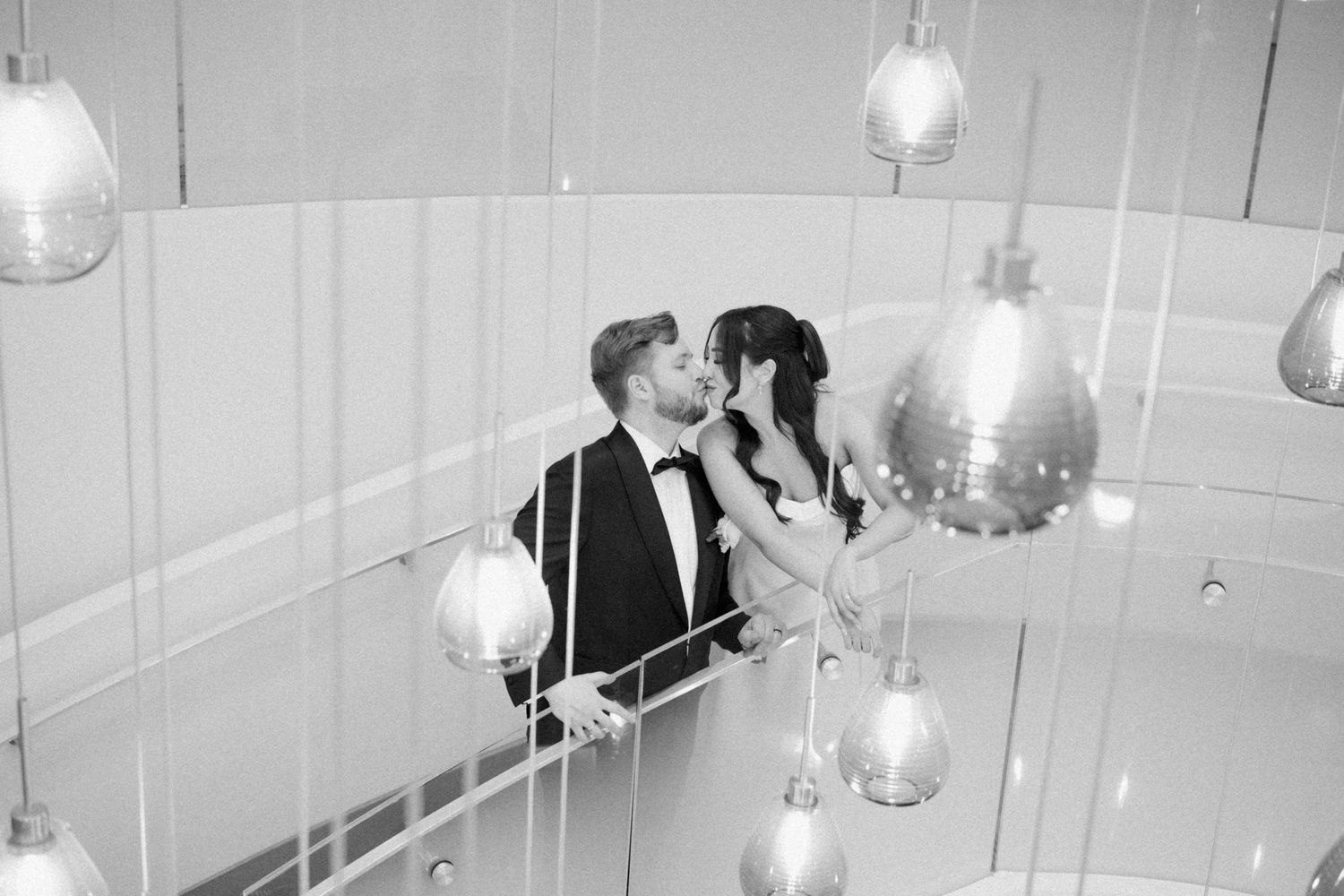 Artistic black and white photo of couple surrounded by hanging pendant lights.