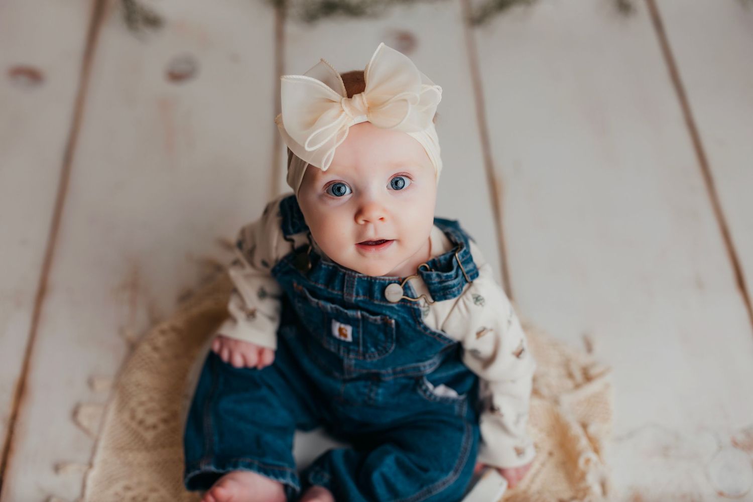 A sweet newborn baby wearing a navy dress with white bow accessories lies on a light colored background.