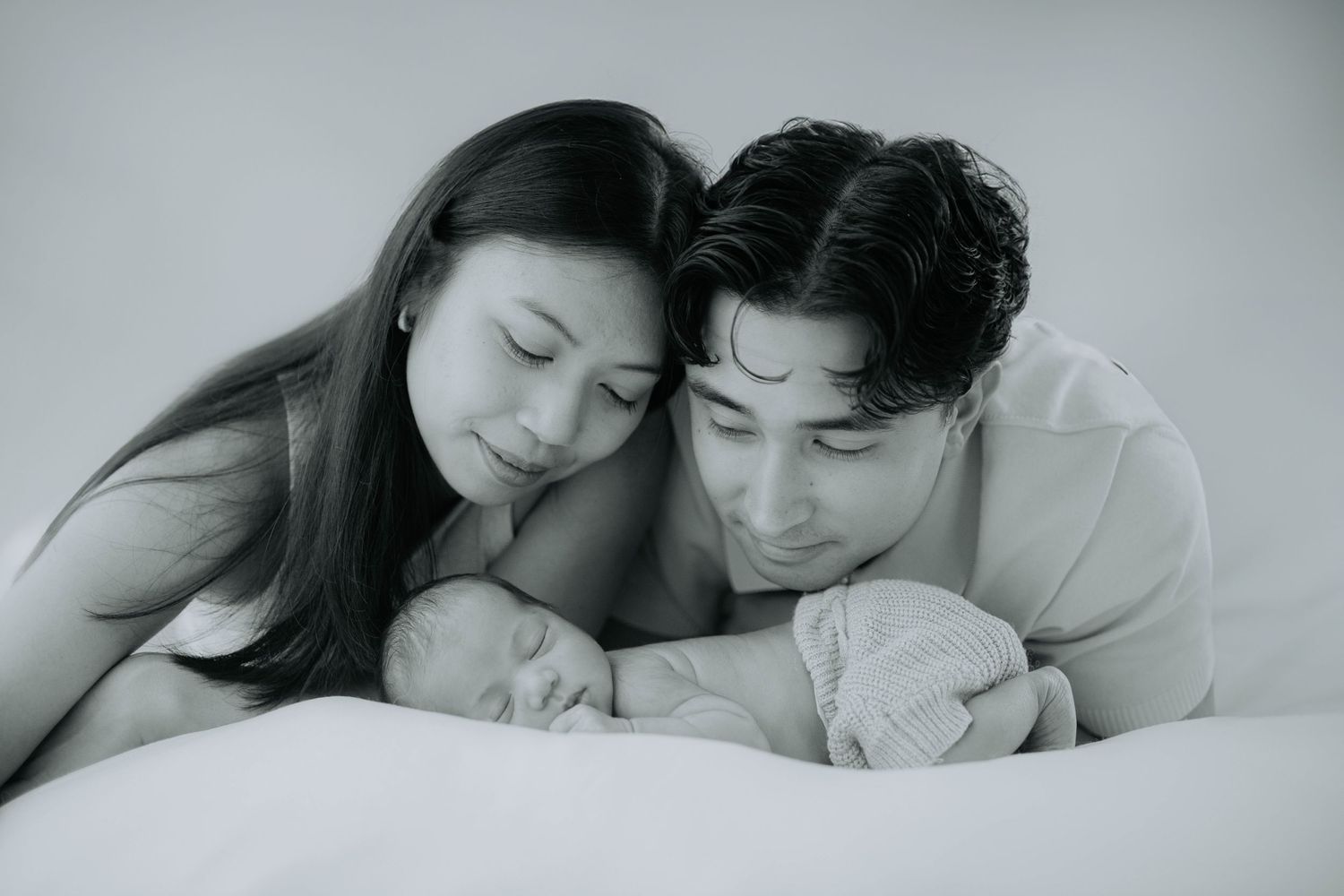 Intimate black and white family portrait with newborn baby on bed.