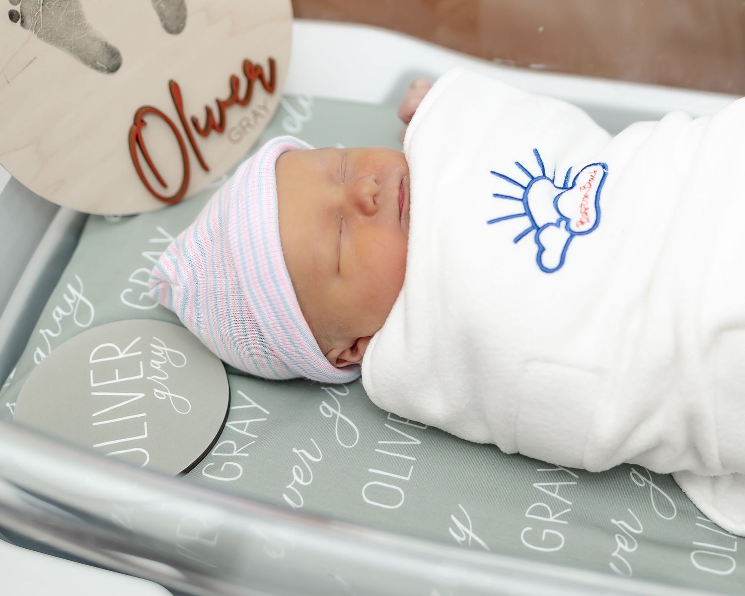 Sleeping newborn in hospital bassinet wrapped in white blanket with blue sun drawing.