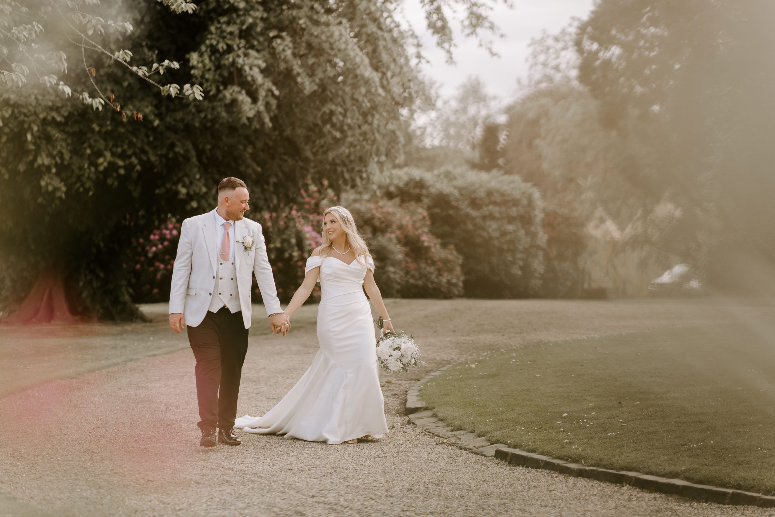 A bride and groom share tender moments in a golden sunset-lit garden setting during their wedding photoshoot.