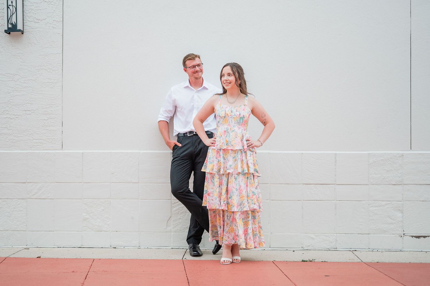 A couple poses casually against a white wall, with the woman wearing a pink tiered maxi dress.