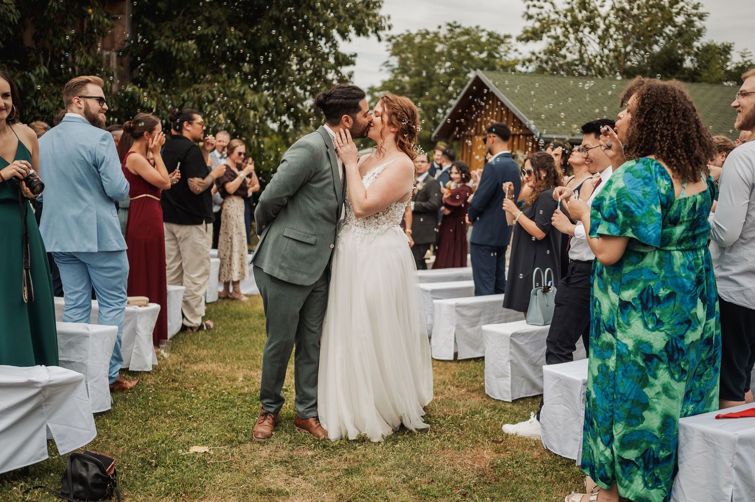Wedding guests celebrate outdoors during a summer ceremony with white chairs arranged on a grassy lawn.