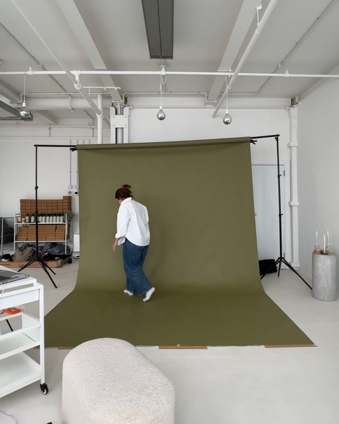 Photographer in black crouches with a vintage camera against white background.