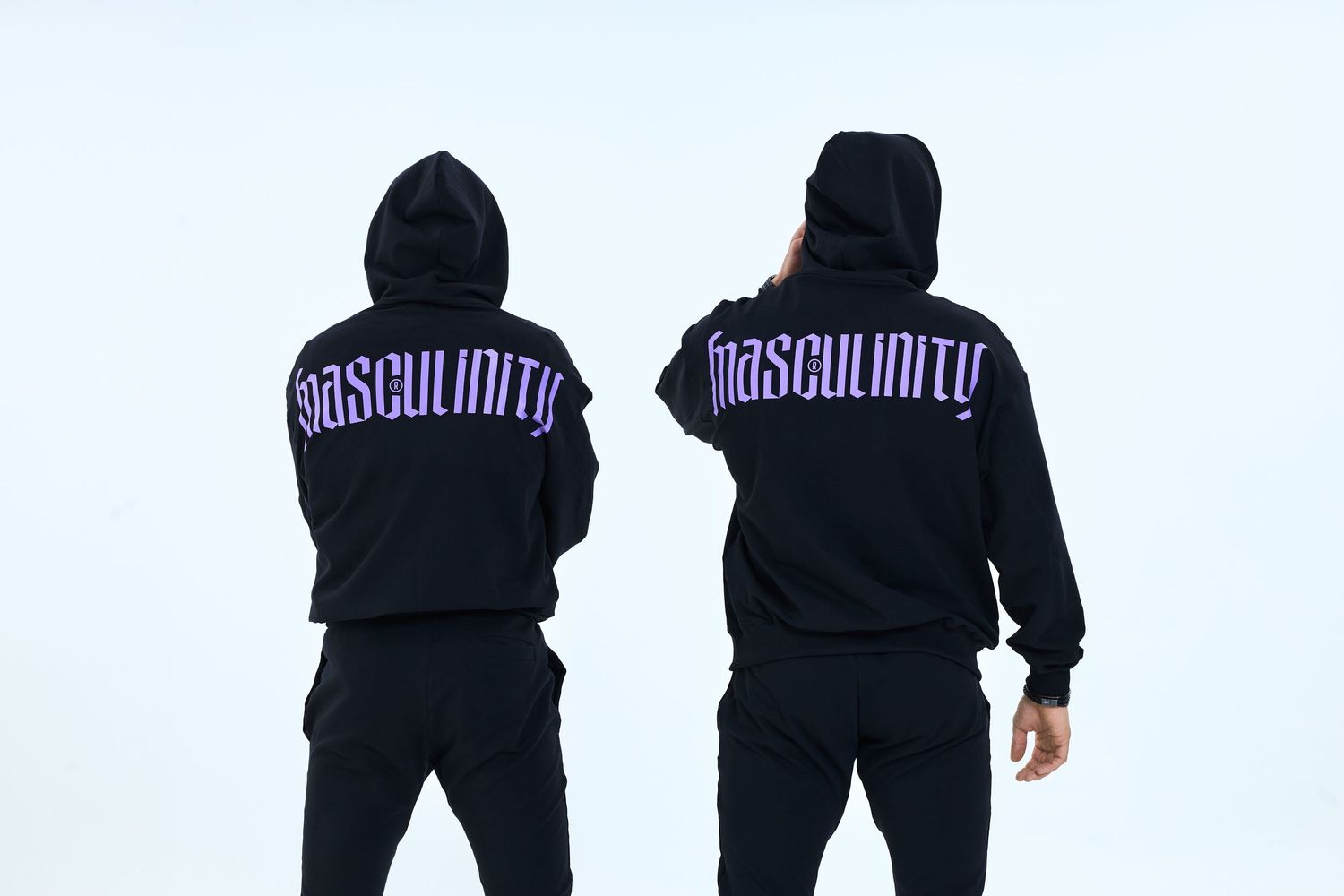 Two people wearing black hoodies with purple Masculinity text on the back, posing against a white background.