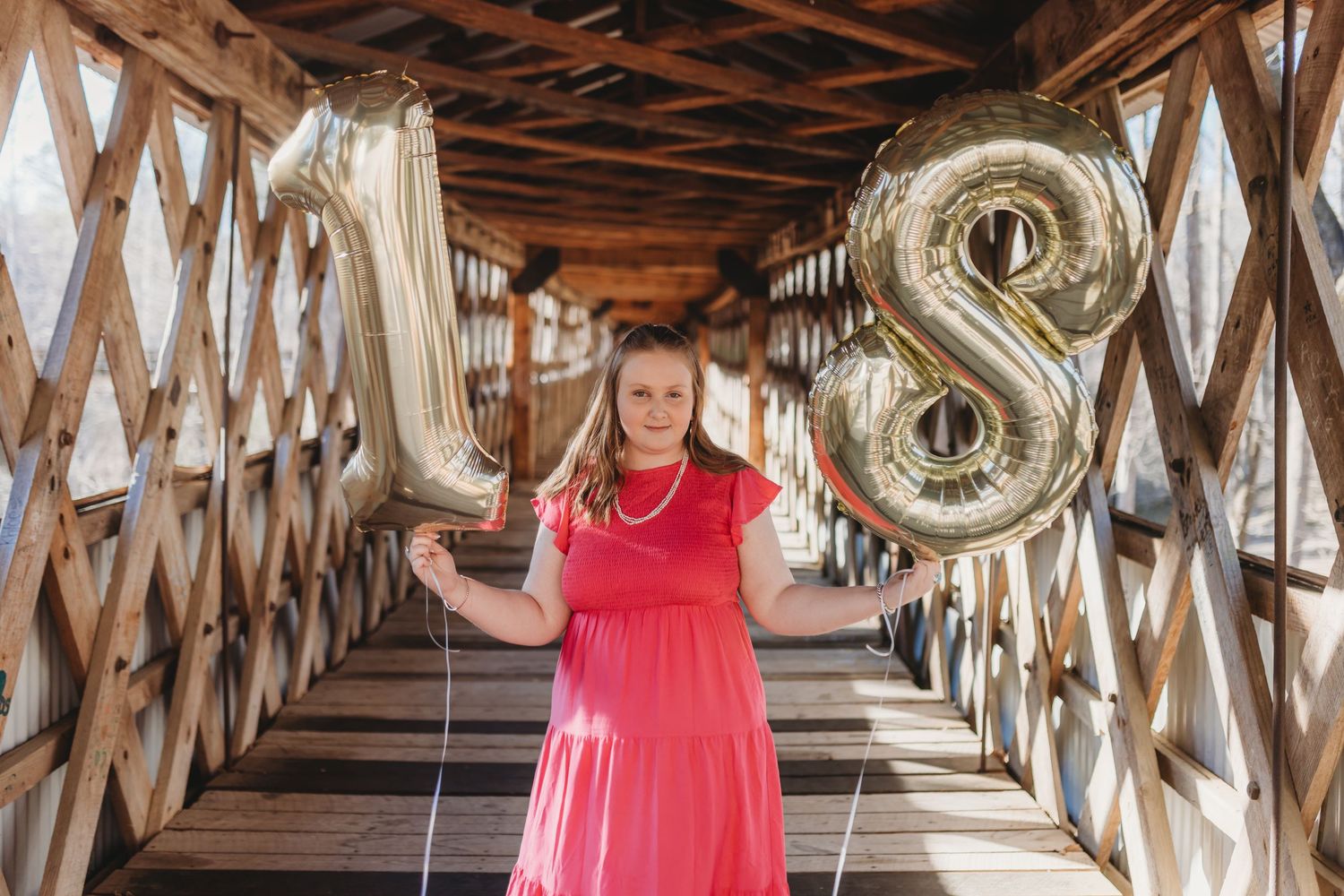 A person in a bright pink dress poses in a rustic wooden hallway with wine barrels lining the walls.
