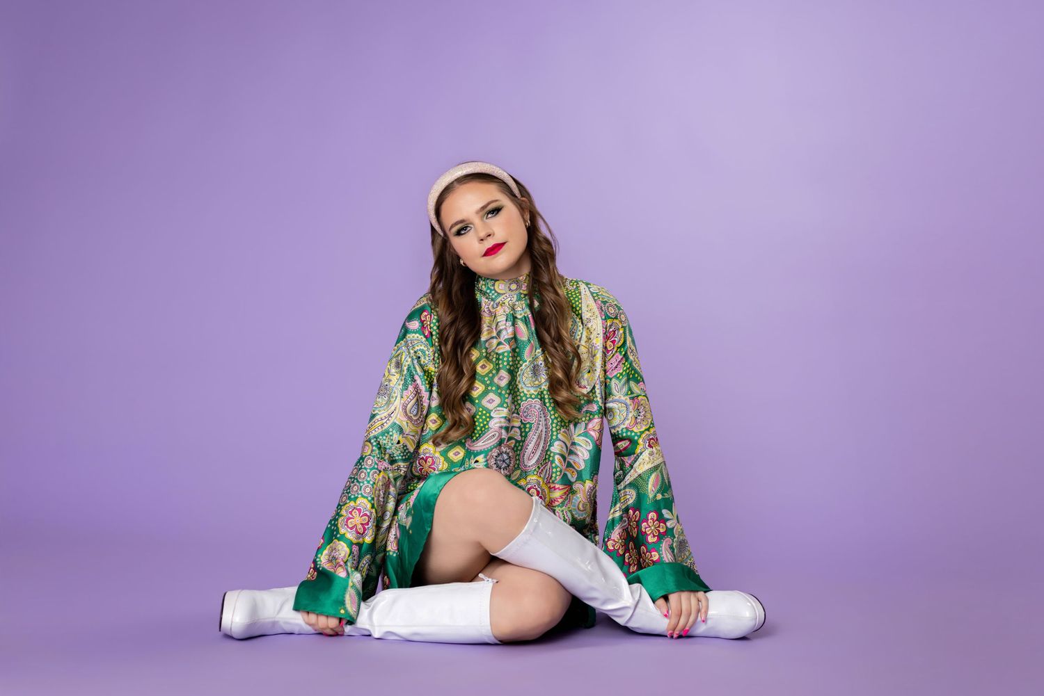 Model wearing a vibrant green floral dress with puff sleeves and embroidered details poses against purple backdrop.