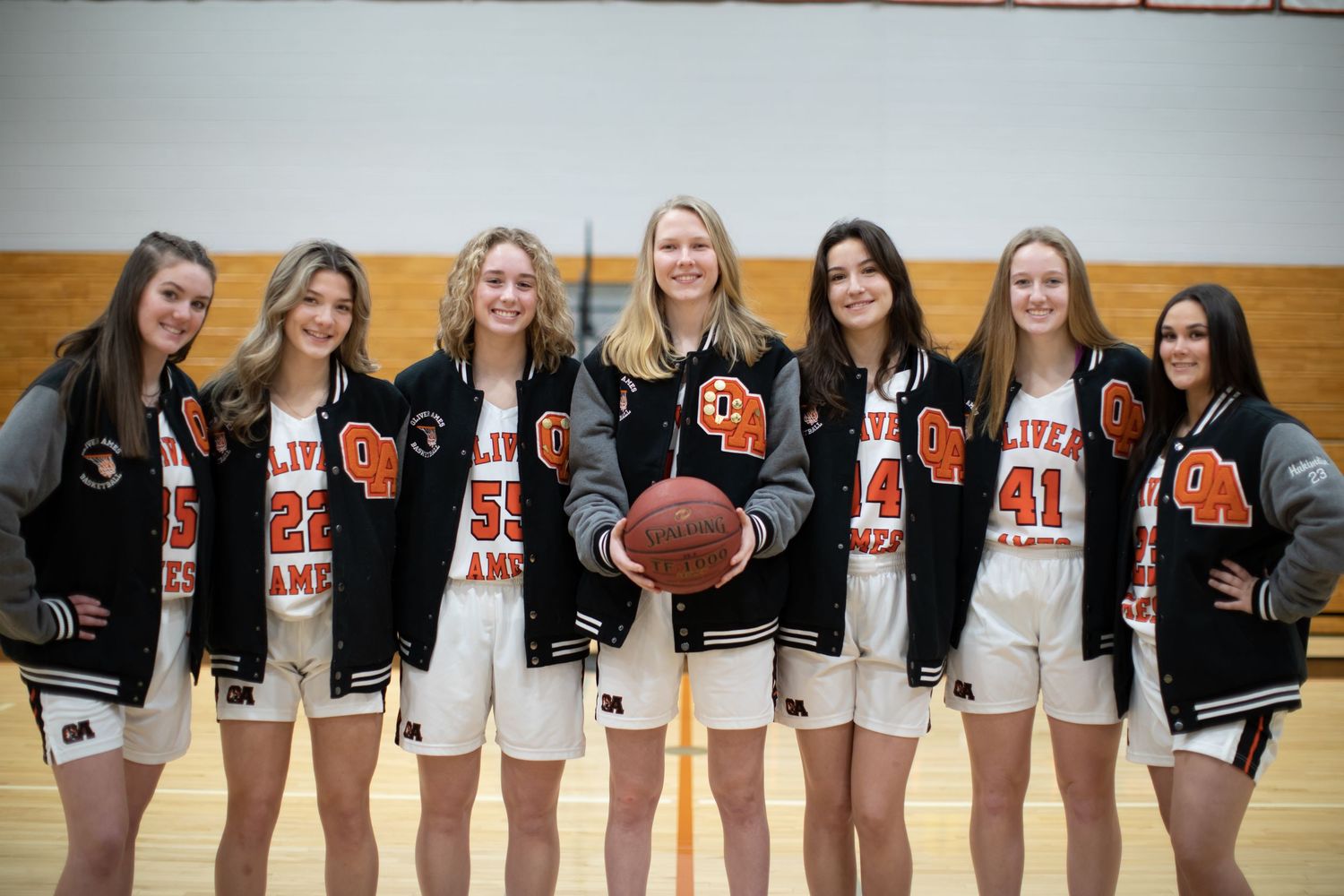 Basketball team members pose together wearing matching varsity jackets and uniforms.