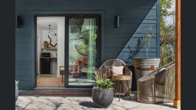 Modern porch with rattan furniture and potted plants featuring glass door reflections.