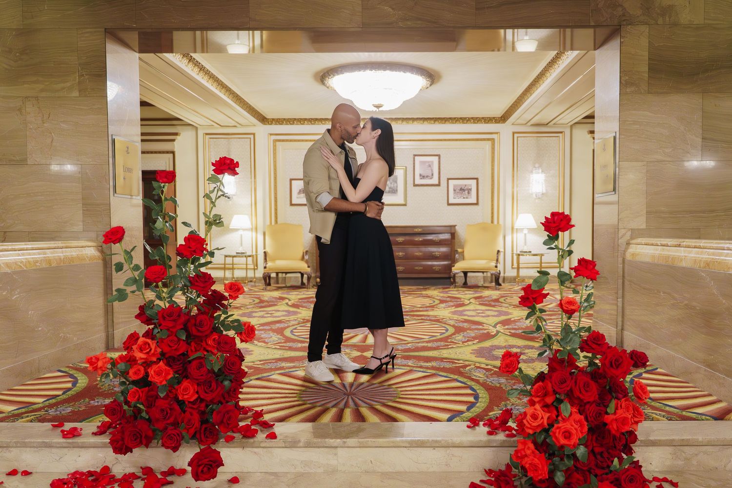 Elegant hotel lobby interior with beige marble floors and bright red rose floral arrangements displayed along the hallway.