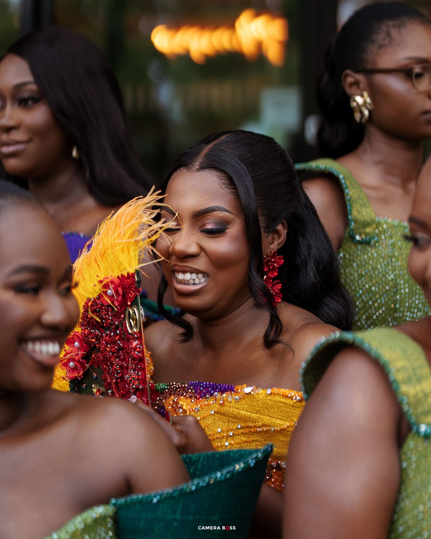 Women in colorful African attire and beaded accessories smile at a festive cultural celebration.