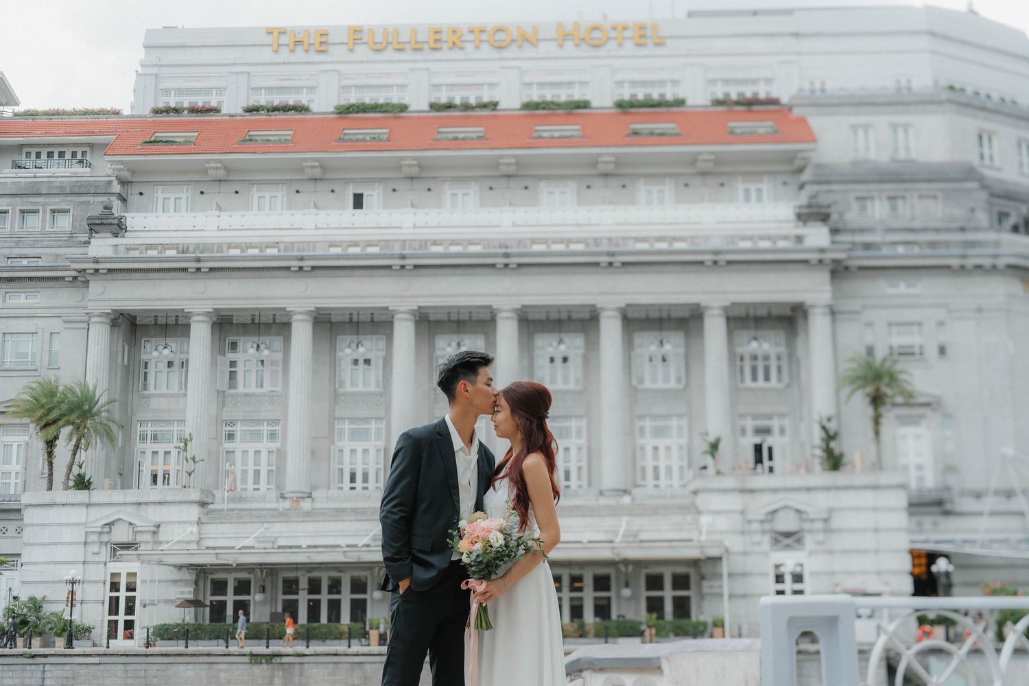 A couple poses in front of the iconic white facade of the Fullerton Hotel in Singapore on their wedding day.