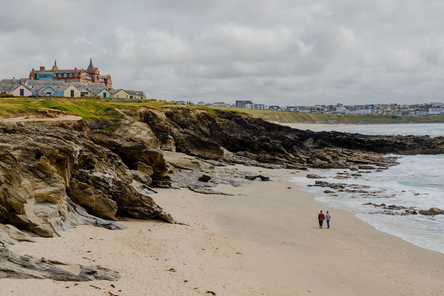 gay couple walking on little Fistral in Newquay with rocky shores and ocean waves