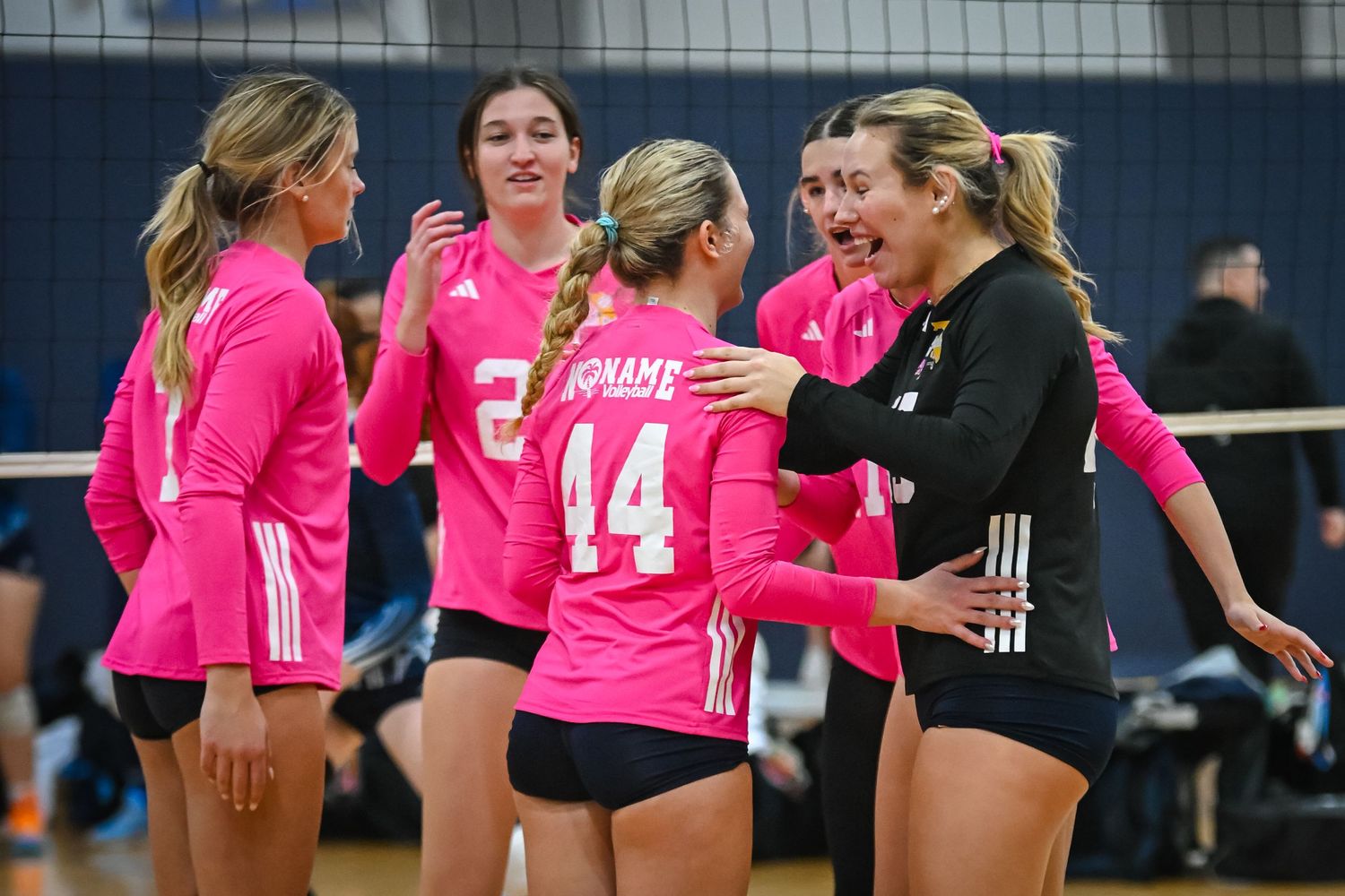 Female volleyball player #20 sets the ball during an indoor tournament match while teammate #33 prepares to spike.