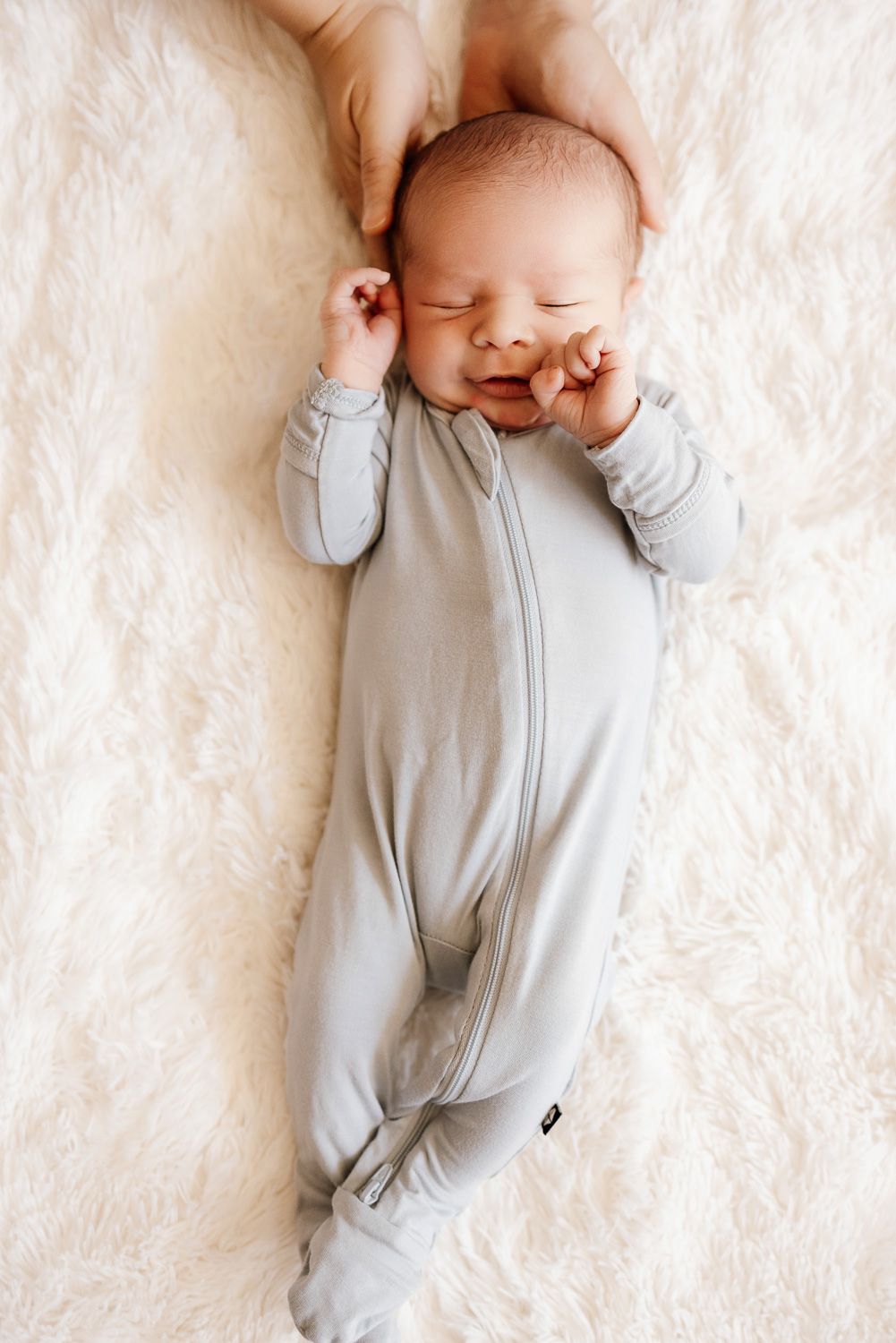 Sleeping baby with mom's hands cradling his head at in-home newborn photography session in San Jose