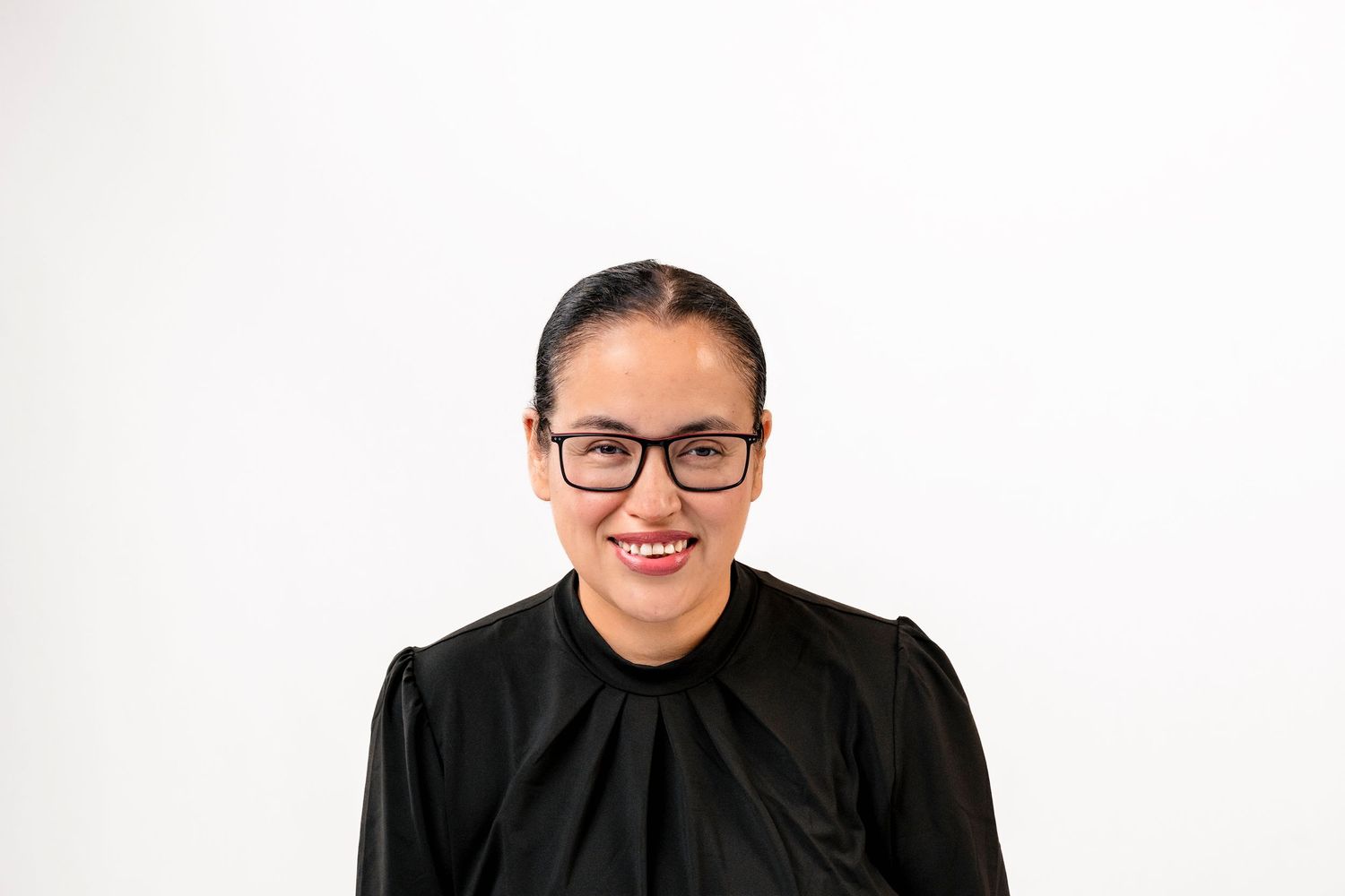 Professional woman in black top and glasses posing confidently against a white background.