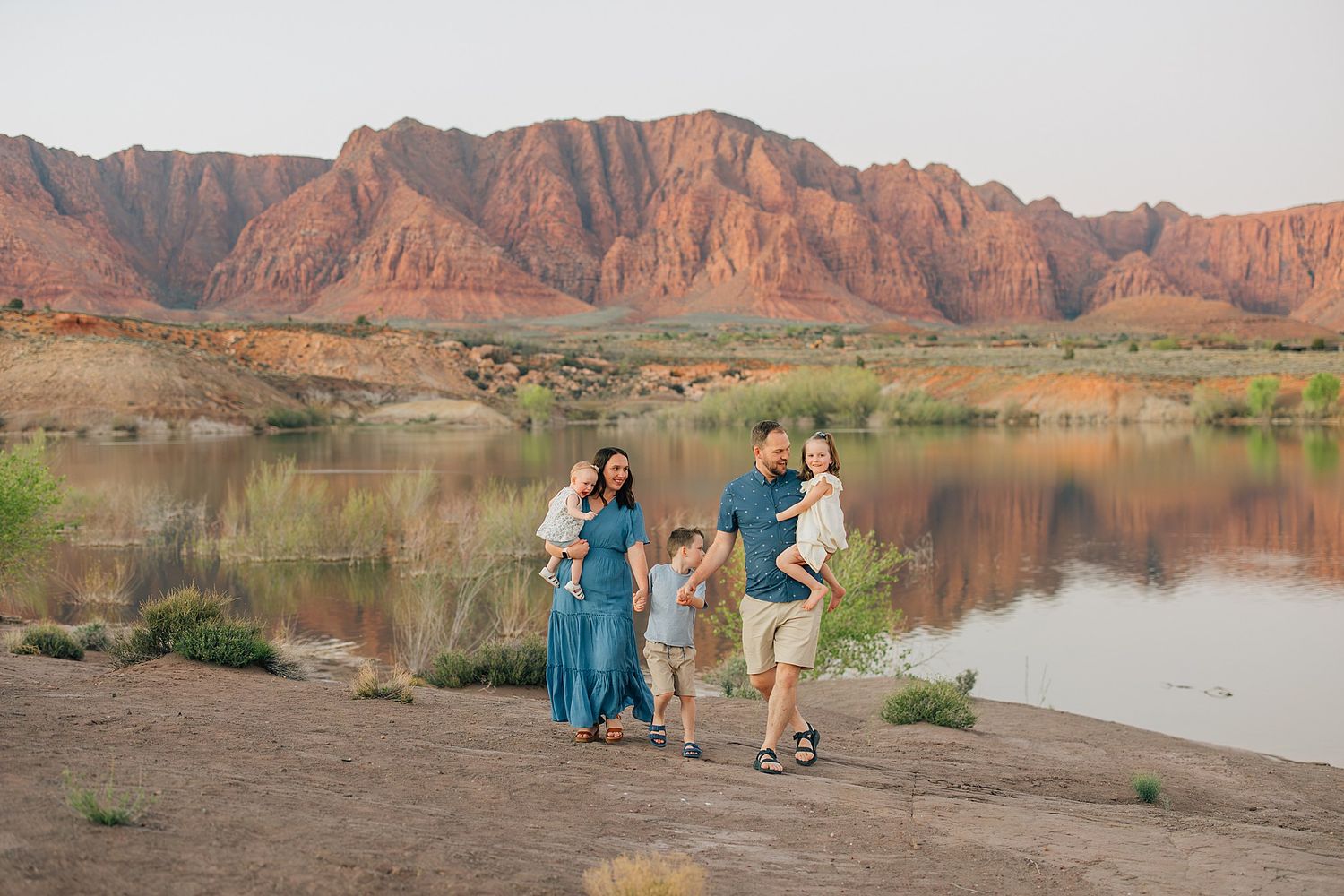 Family of five walking by a scenic red rock canyon lake at sunset in St. George, Utah.