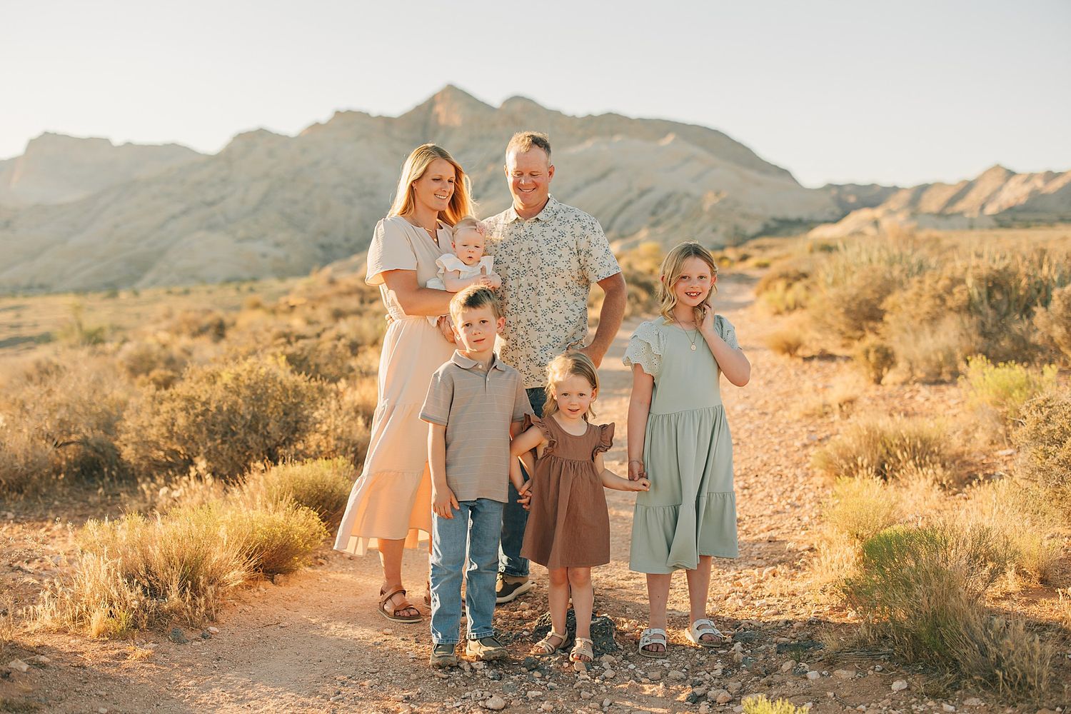Family of five posing outdoors in desert landscape with mountains at golden hour.
