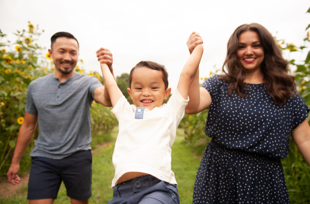 Family of four splashing and holding hands in a shallow creek surrounded by lush green trees.