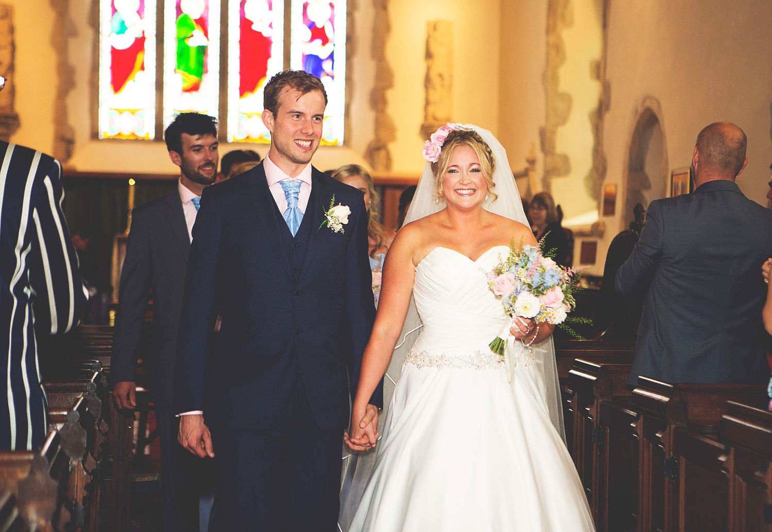 Bride and groom walk down church aisle after wedding ceremony, bride holding bouquet during surrey wedding photos
