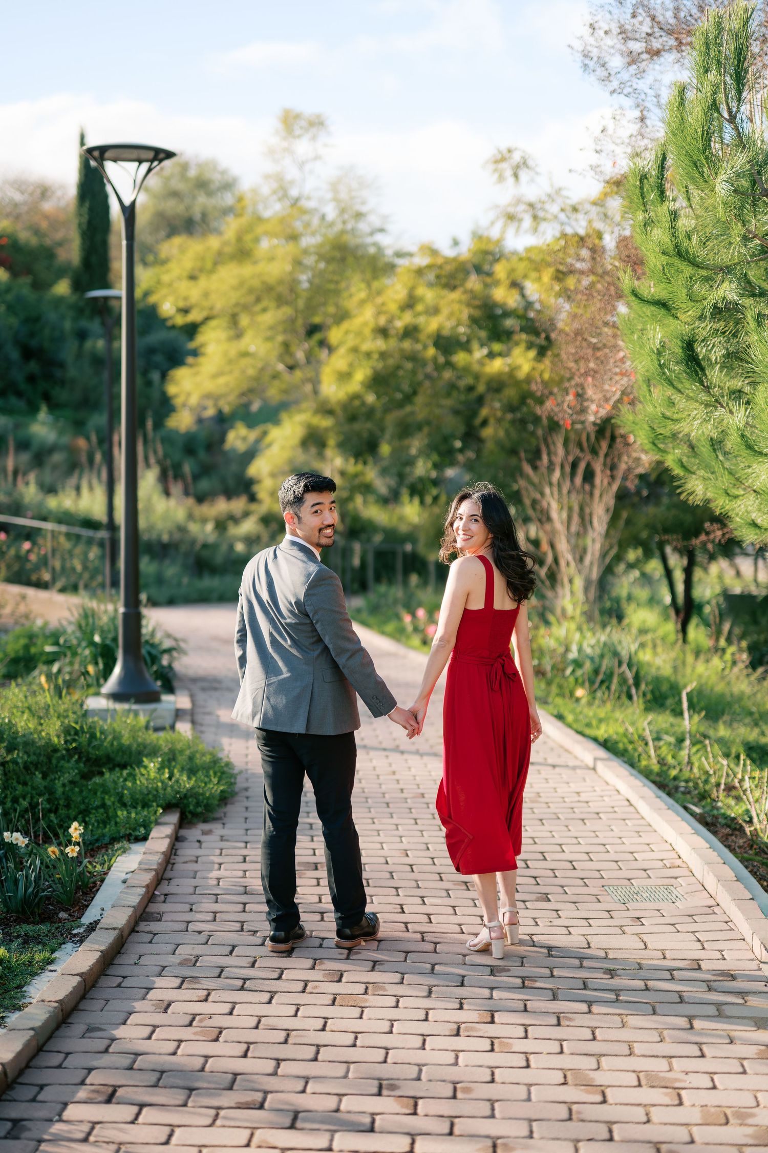 A romantic outdoor photoshoot in a sunlit park with green grass and trees creating a dreamy natural backdrop.