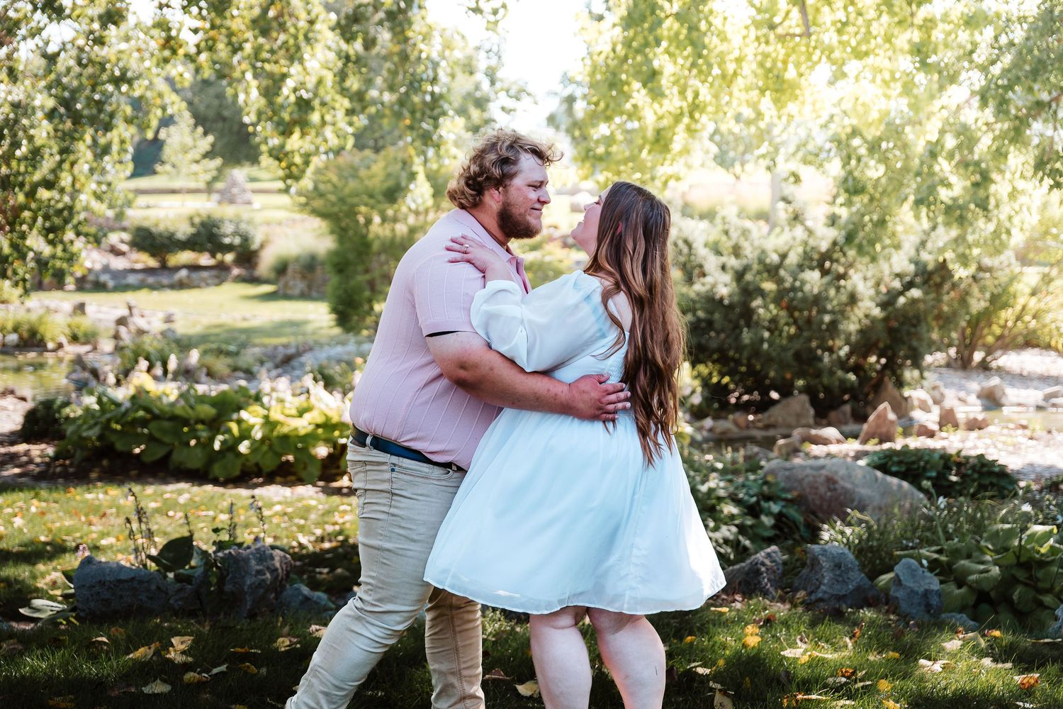 Couple sharing a romantic moment dancing outdoors in a lush green garden park setting on a sunny day.