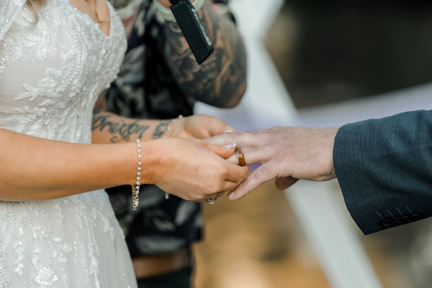 Bride with tattoos placing a wedding ring on groom's finger during ceremony.