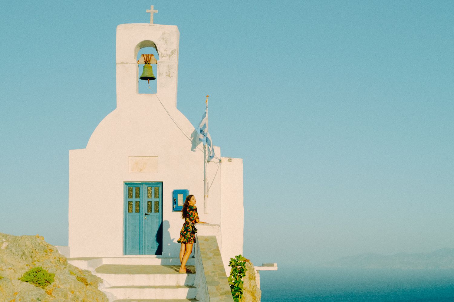 Whitewashed chapel with blue doors and bell tower under a clear Aegean sky.