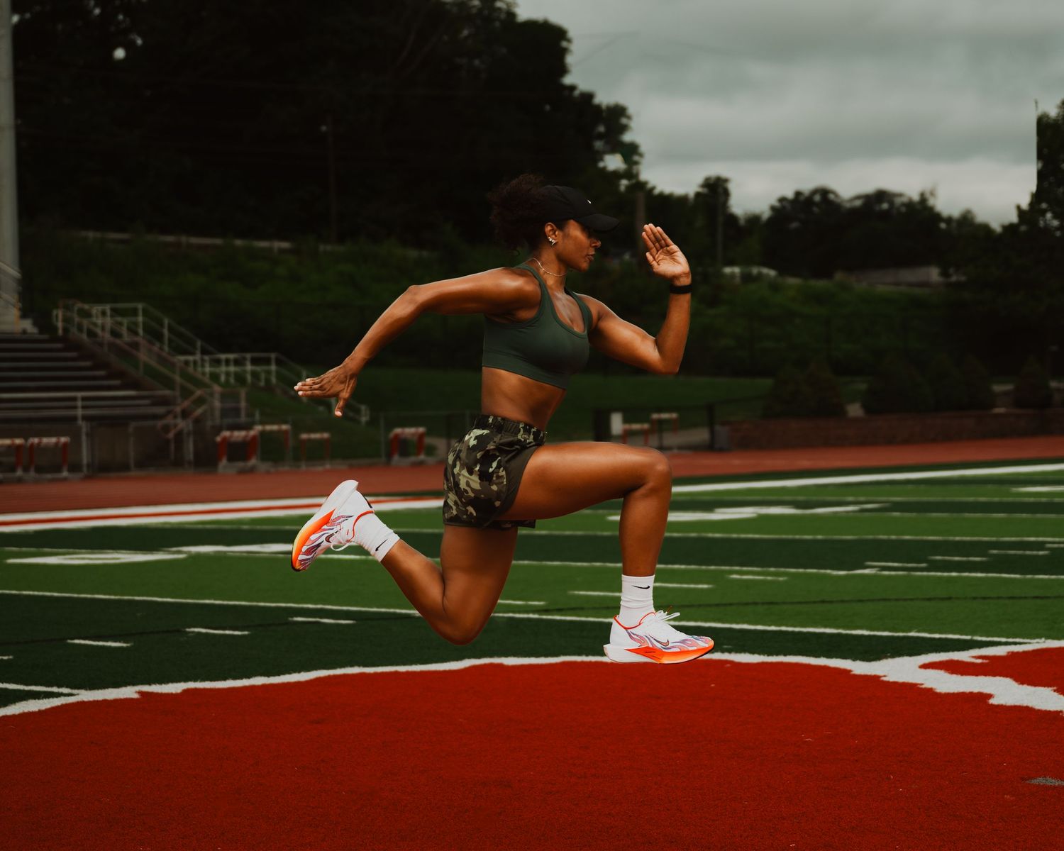 An athlete in motion sprinting on a red track in dynamic form wearing black shorts and white sneakers.