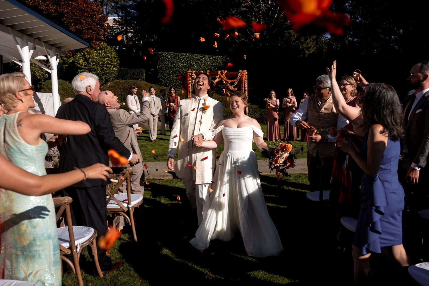 Wedding guests dance and celebrate outdoors during a festive garden reception in the evening sunlight.