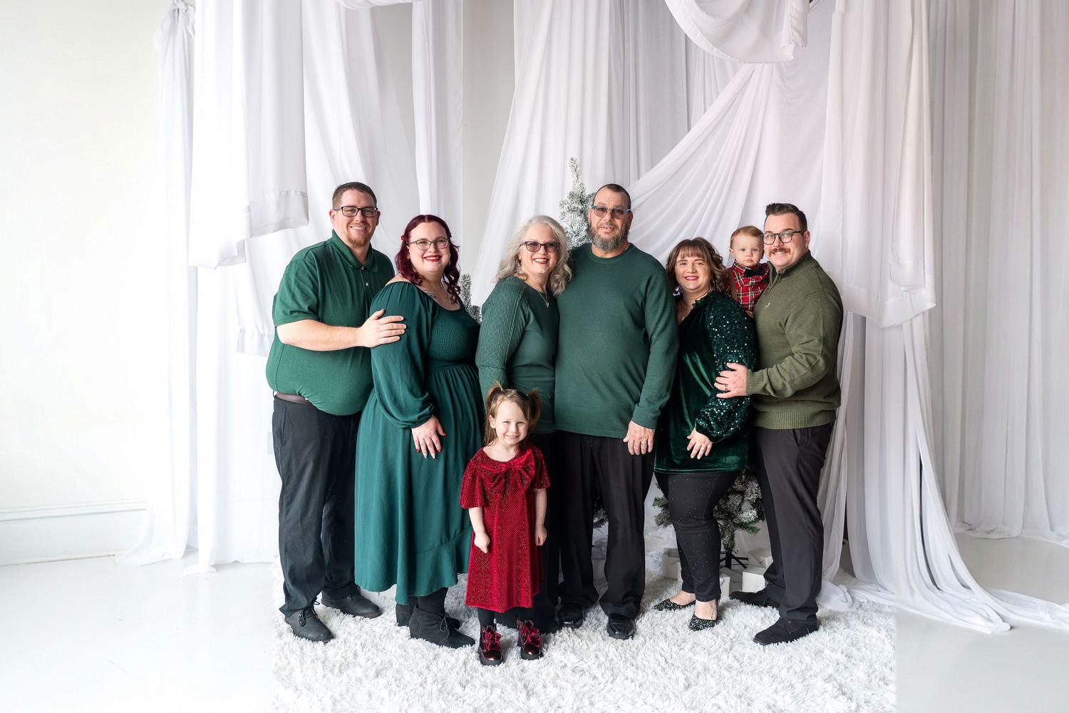 Large family in green and red outfits posing together in front of white draped backdrop.