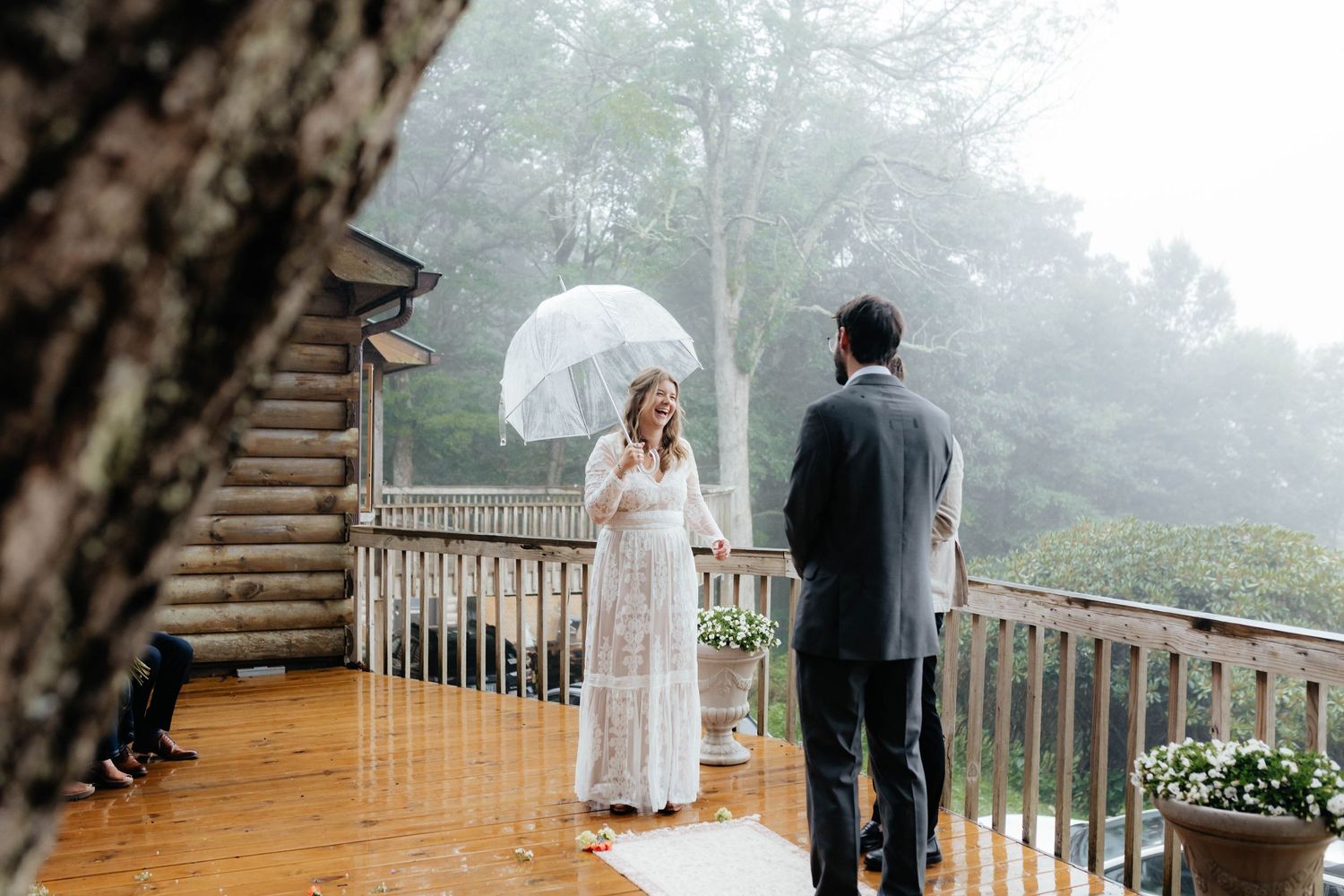 A couple shares an intimate moment on a misty wooden deck during a rainy wedding ceremony.