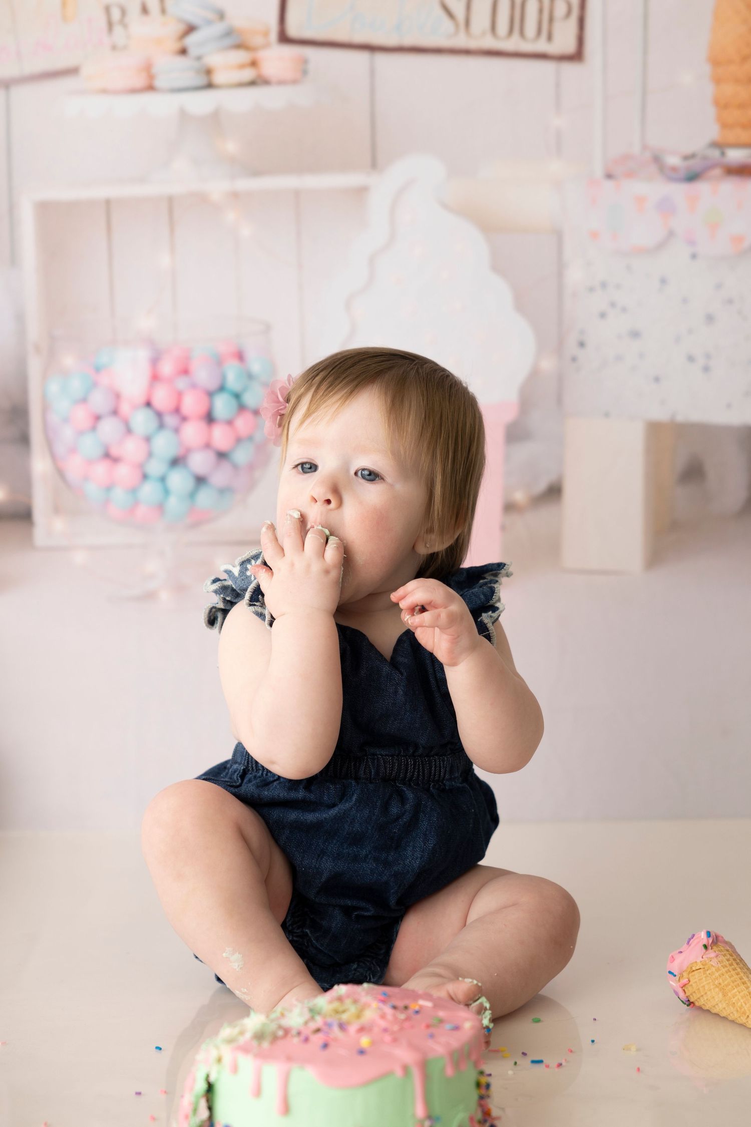 Baby in navy blue outfit sits on floor with pink and blue decorations during cake smash photo session.
