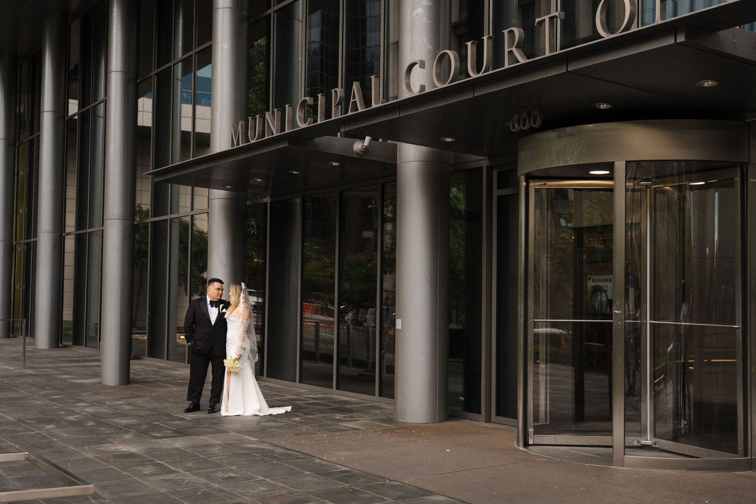 A couple in wedding attire stands at the entrance of the Municipal Court of Ohio building.