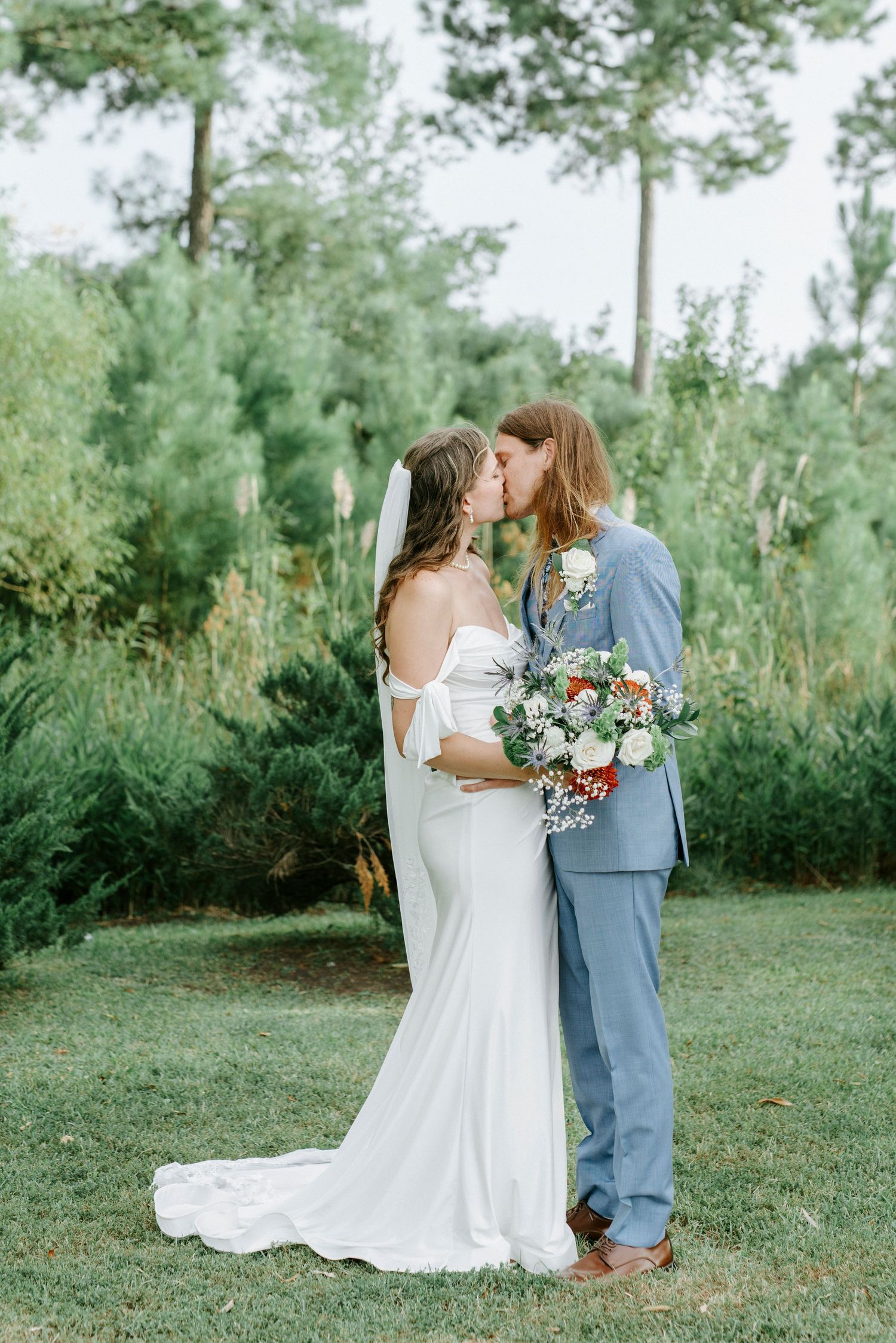Newlywed couple shares intimate moments during garden ceremony with floral bouquet of white roses and greenery.