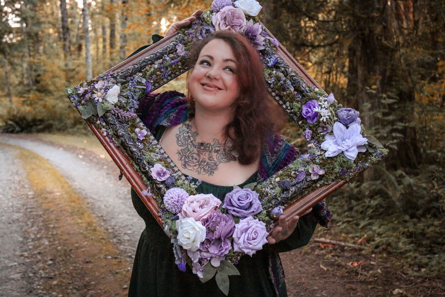 A decorative floral frame adorned with purple and pink roses held up on a forest path during autumn.