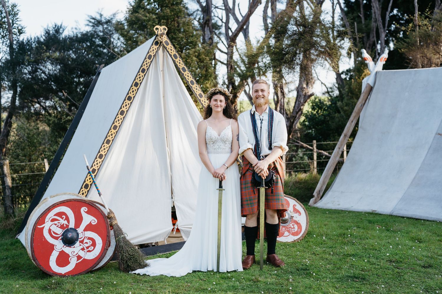 A wedding couple poses in front of white teepee tents decorated with red hearts during an outdoor ceremony.
