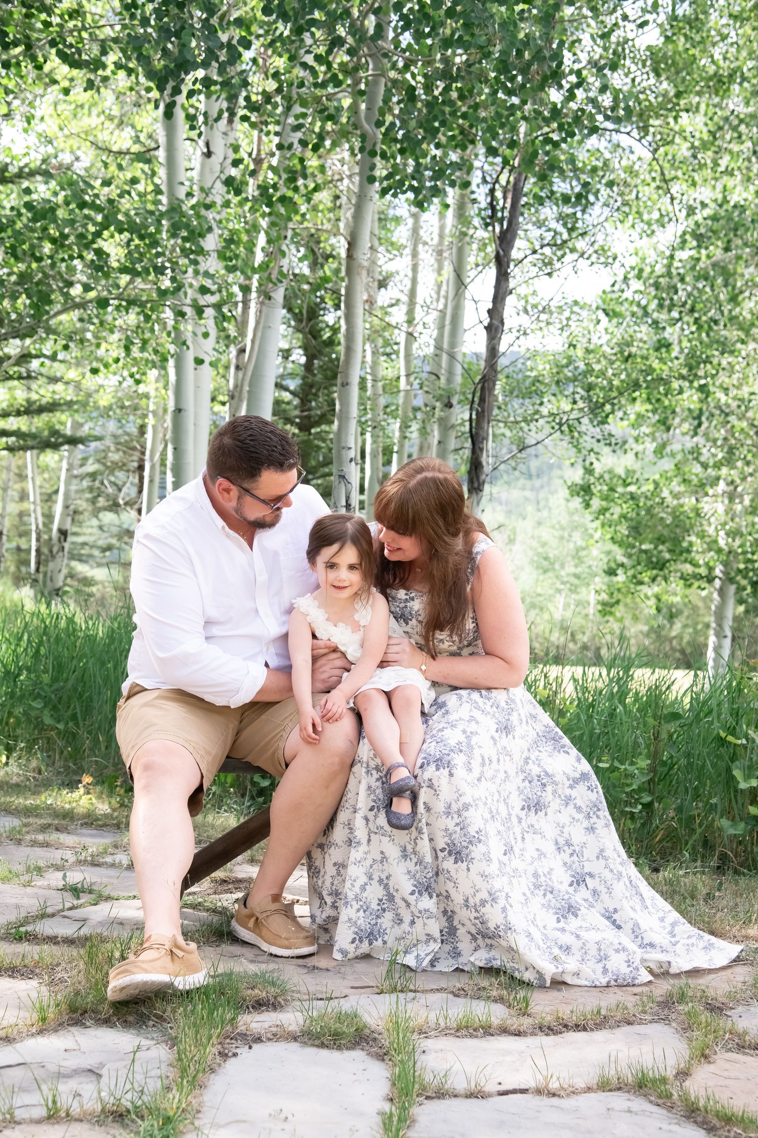 Family sitting together on stone steps surrounded by aspen trees in a natural outdoor setting.