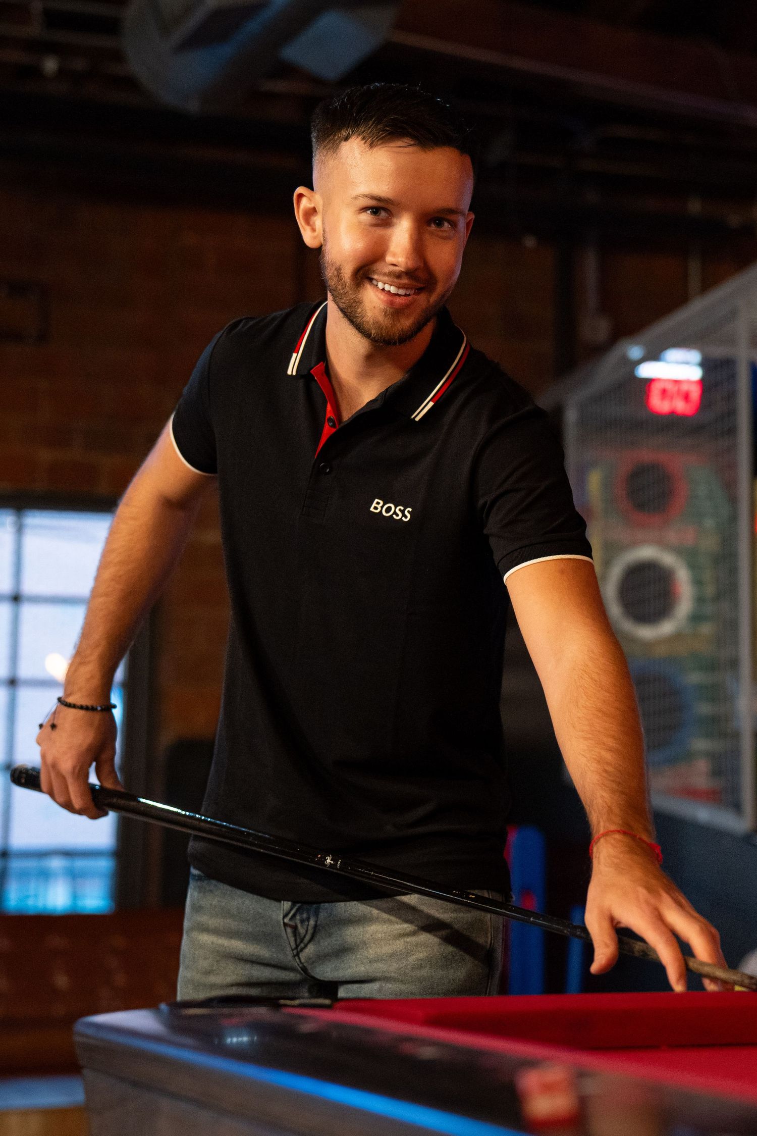Someone in a black polo shirt takes aim while playing pool at a bar with exposed brick walls and neon lighting.