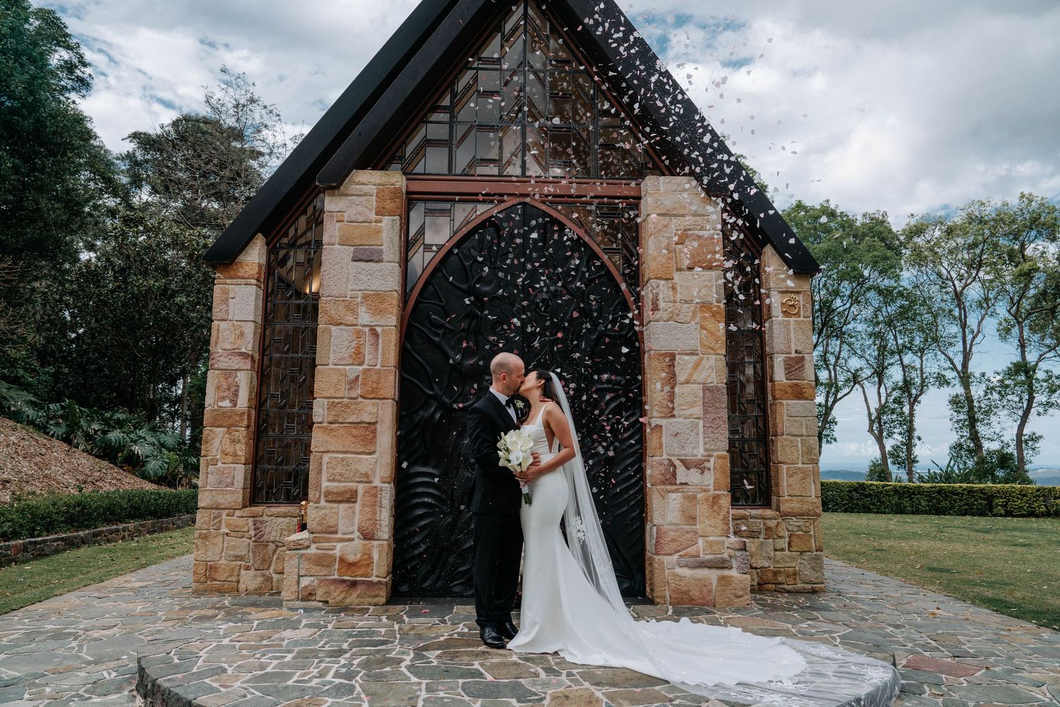 A couple embraces under a rustic stone archway during their wedding ceremony on an overcast day.