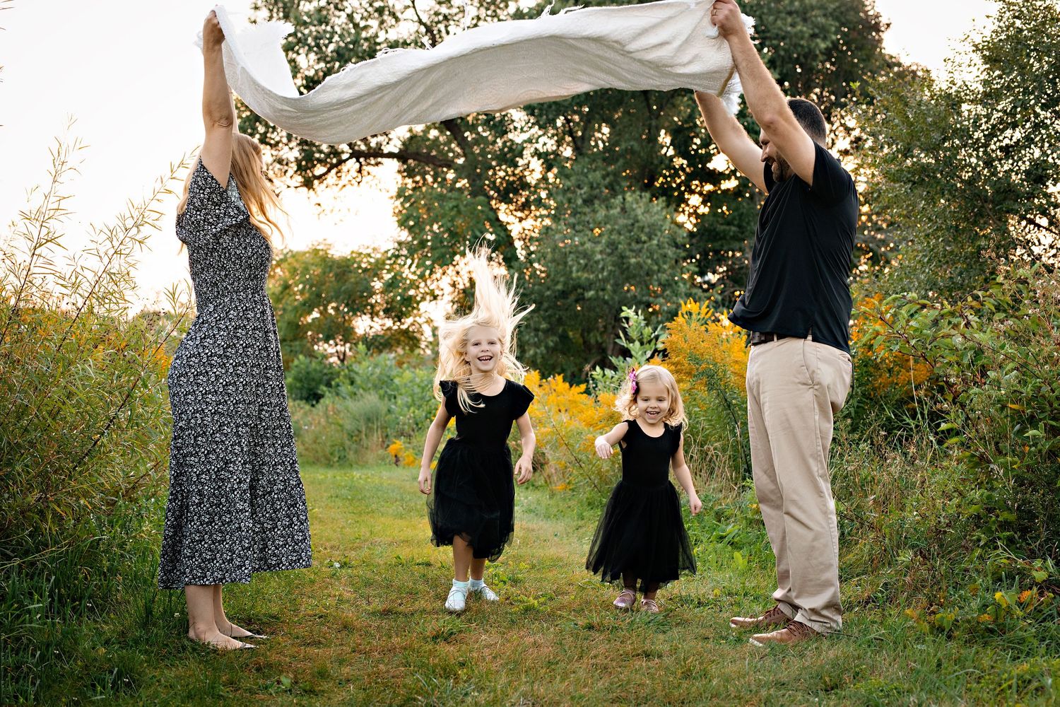 A group dances together in a field at sunset with white fabric flowing in the breeze.