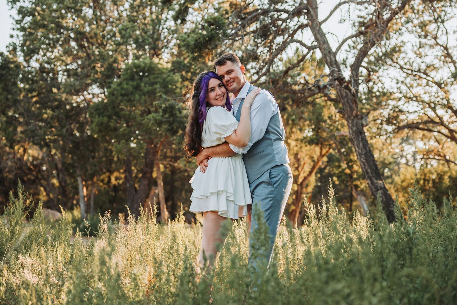 A couple shares tender moments during a golden hour photoshoot in a rustic outdoor setting with tall grass and trees.